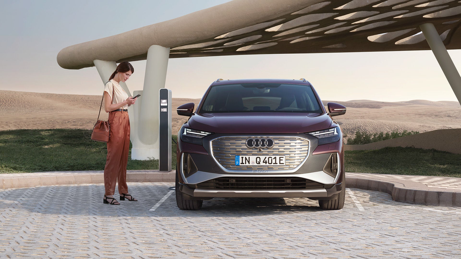 Audi Q4 e-tron som laddas vid en laddstolpe, en kvinna med en mobil i handen står bredvid