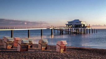 Strandkörbe an der Ostseeküste in Timmendorf mit Seebrücke und Pavillon im Abendlicht.