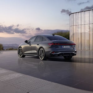 Die schwarze Edition One mit Akzenten in Magnesiumgrau der A5 Limousine in schrägen Heckprofil spiegelt sich in dem glatten Untergrund. Im Hintergrund sind Berge bei Dämmerung zu sehen.