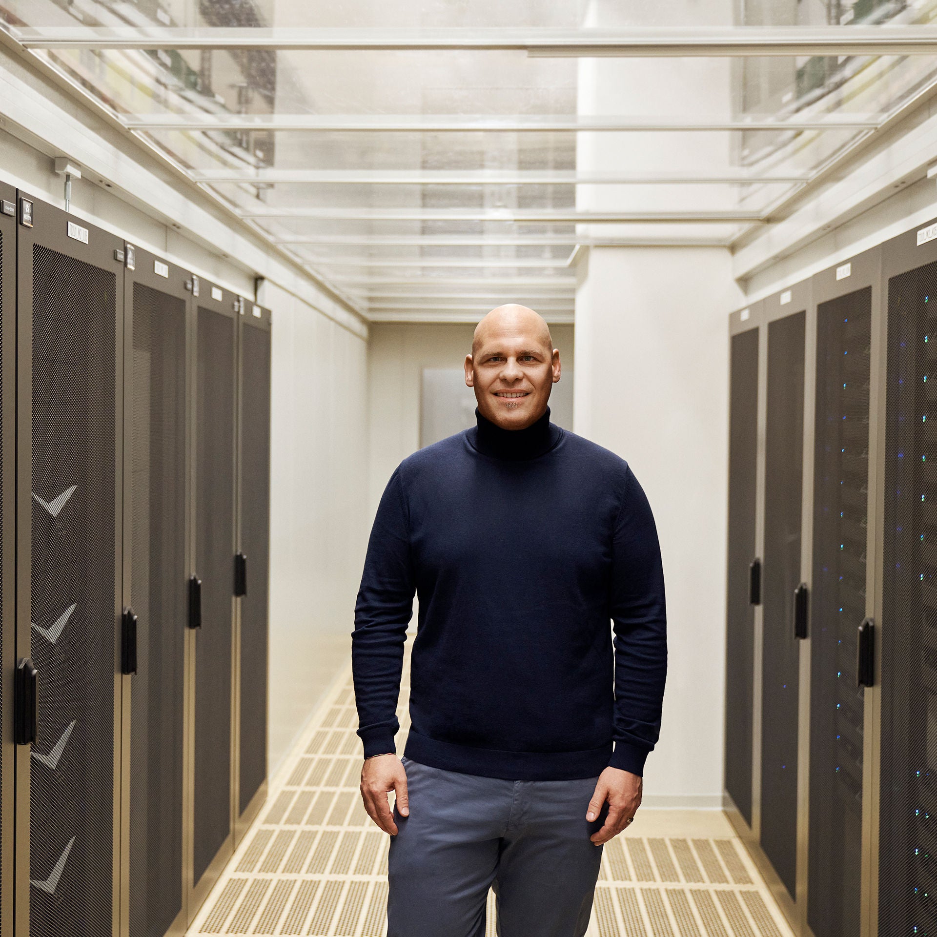 Sebastian steht in einem Serverraum zur Kamera gerichtet und lächelt