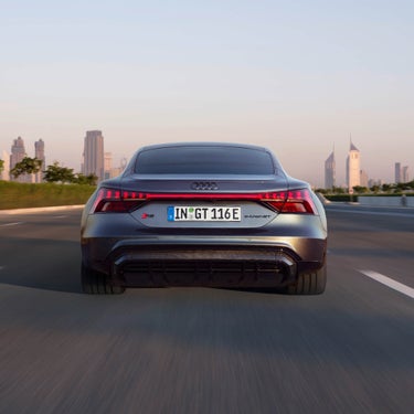 Rear view of a moving Audi RS e-tron GT on a road with city skyline in the background.